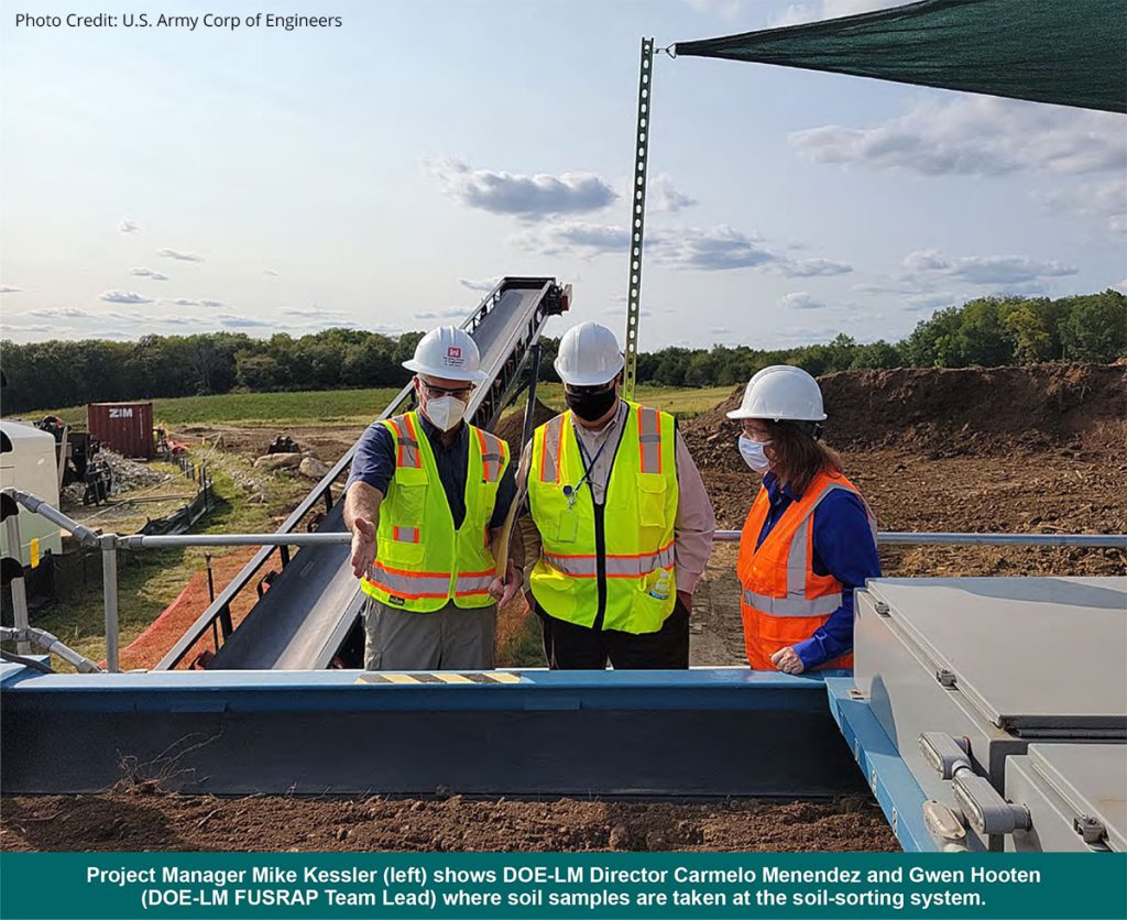 roject Manager Mike Kessler (left) shows DOE-LM Director Carmelo Menendez and Gwen Hooten (DOE-LM FUSRAP Team Lead) where soil samples are taken at the soil-sorting system.